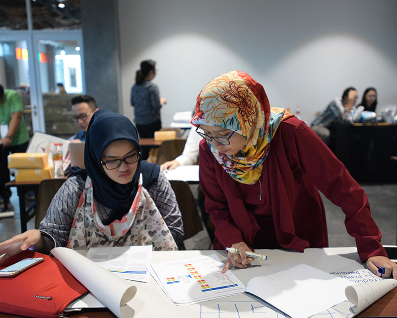 Two women in headscarves looking down at charts and papers in an open office setting