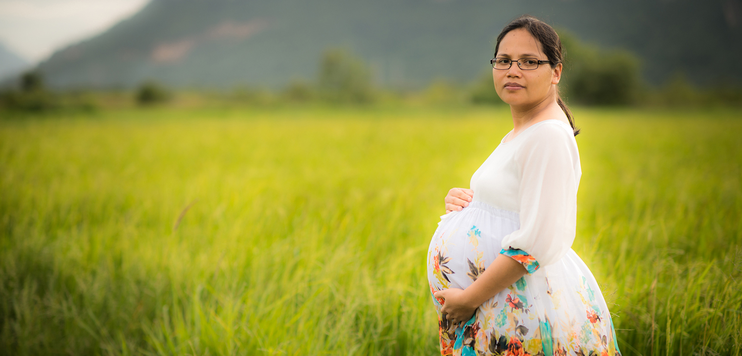 Pregnant Asian woman holding her belly standing in a field