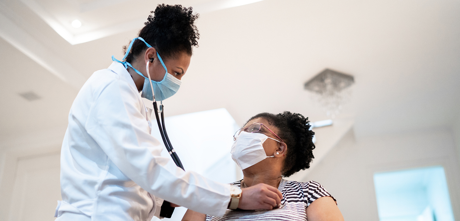 Doctor listening to patient's heartbeat during home visit - wearing face mask