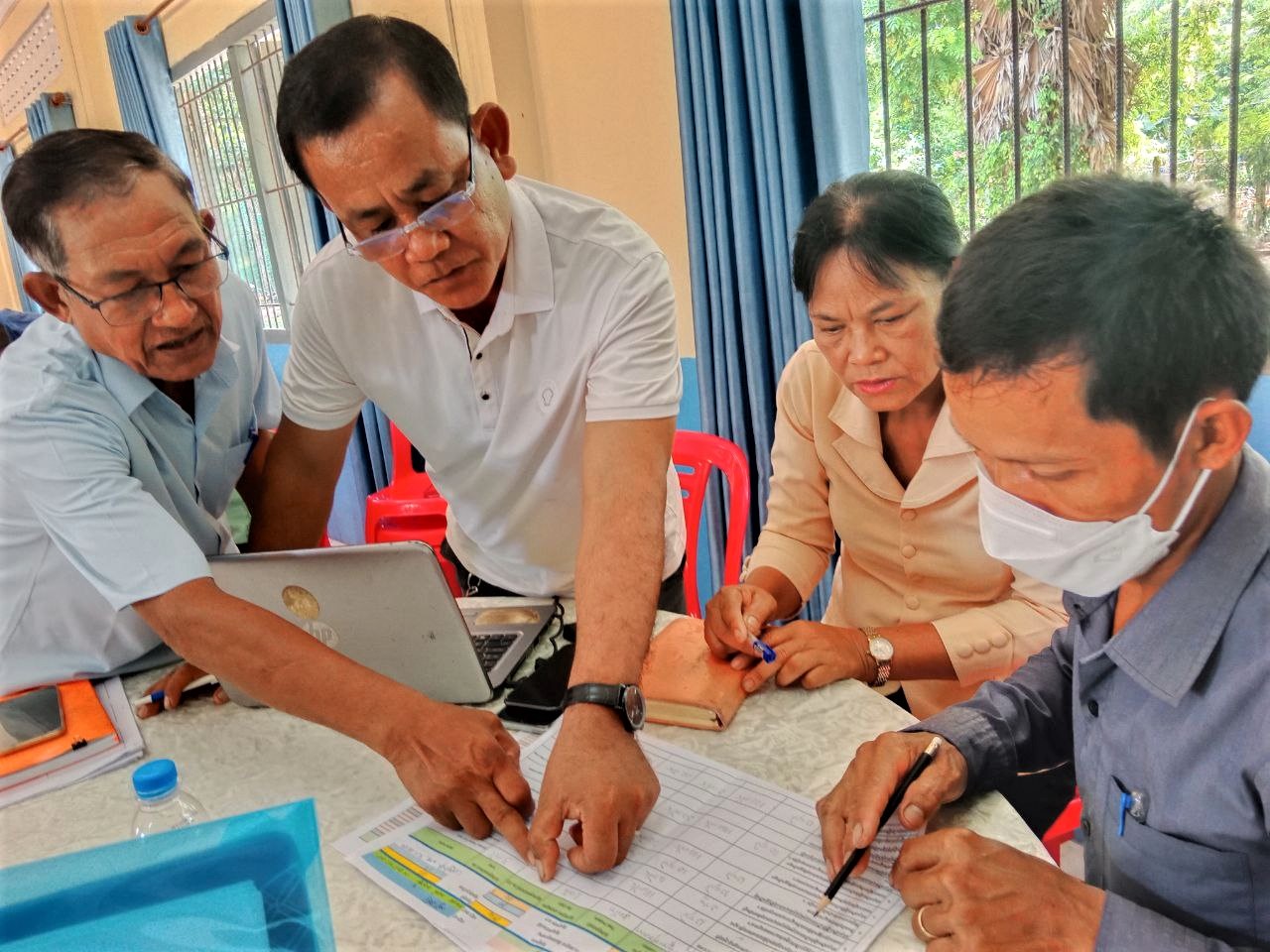 Cambodian men and women around a table pointing at a chart