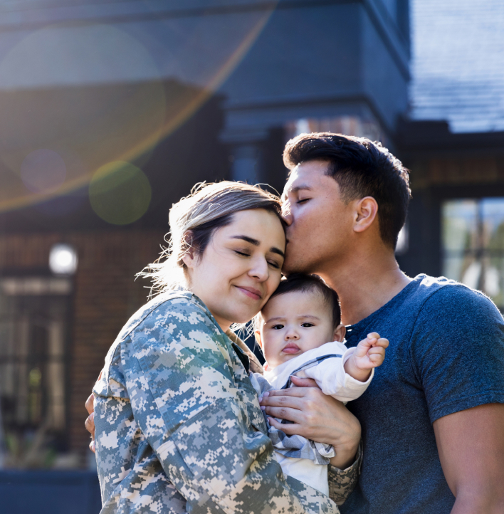 Women in military uniform holding her baby, being kissed by her husband