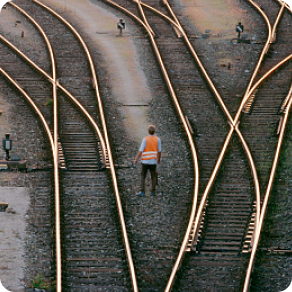 Bird's-eye view of the back of a worker wearing an orange safety vest standing in the train track yard.